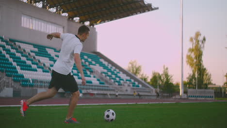 Jugador-De-Fútbol-Pateando-La-Pelota-En-Salto.-Un-Jugador-De-Fútbol-En-Un-Juego-Dramático-Durante-Un-Partido-De-Fútbol-En-Un-Estadio-De-Fútbol-Profesional-Al-Aire-Libre.-Los-Jugadores-Visten-Uniforme-Sin-Marca.